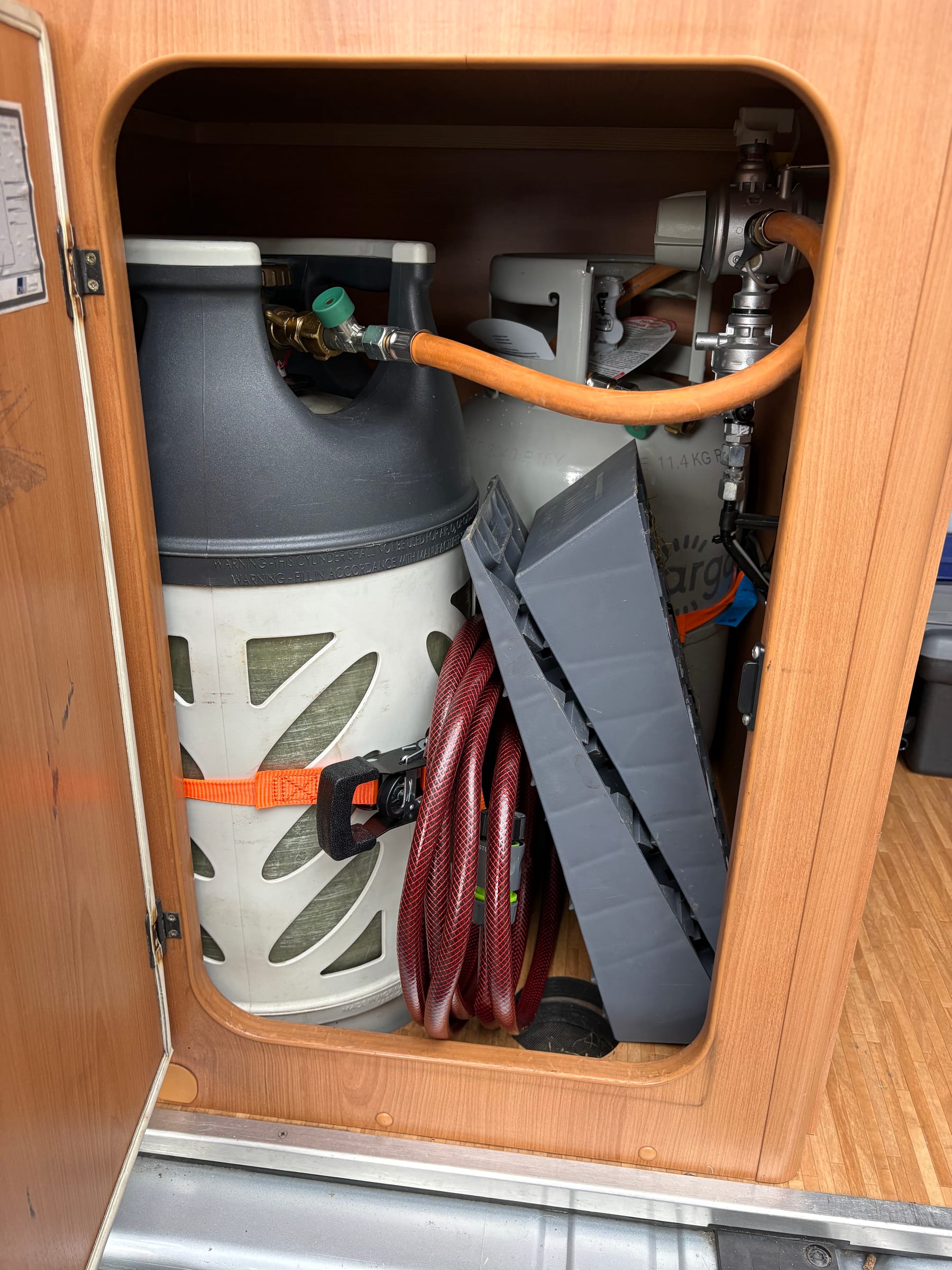 Gashok achterin de camper met gasflessen en tuinslang.